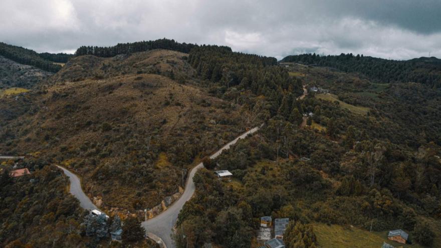 Páramo El Verjón con primer plano de cima de montaña tomada desde dron y que rodeada de árboles la atraviesa una carretera vacía.