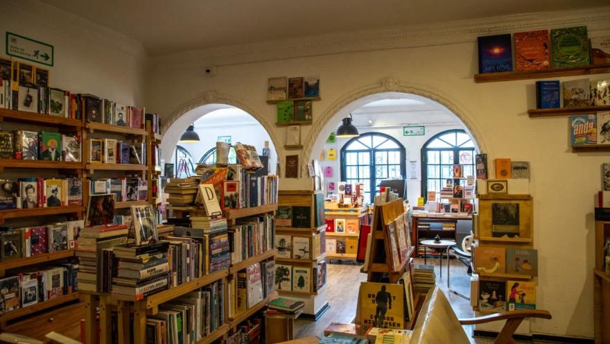 Librería Garabato, sala abarrotada con libros en estanterías en pared y piso. Dos arcos en la pared conducen a otra sala donde se ven más libros y unas ventanas al exterior donde hay luz de día.