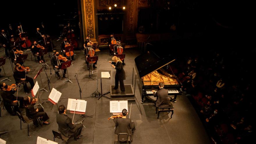 Teatro Colón, view of the stage from a balcony with musicians playing instruments and a conductor directing.