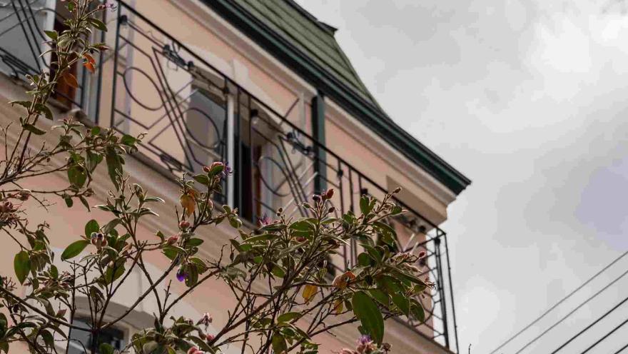 Chapinero con gachada de casa estilo francés con grandes ventanales, techos en arco estilo art deco, y ramas de flores que la tapan.
