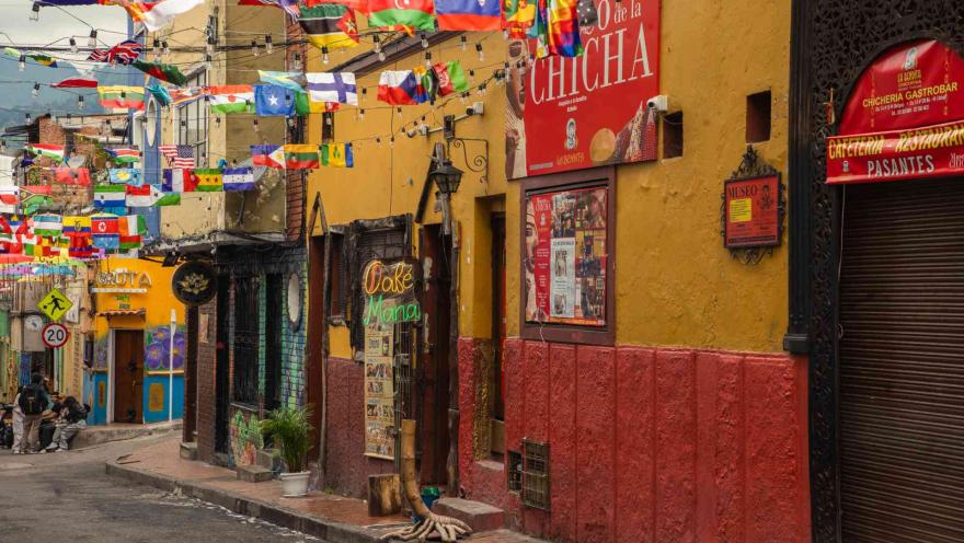 Plazoleta del Chorro de Quevedo en calle circundante decorada con banderas de países y con establecimentos de venta de chicha. Hay algunas personas en una esquina.