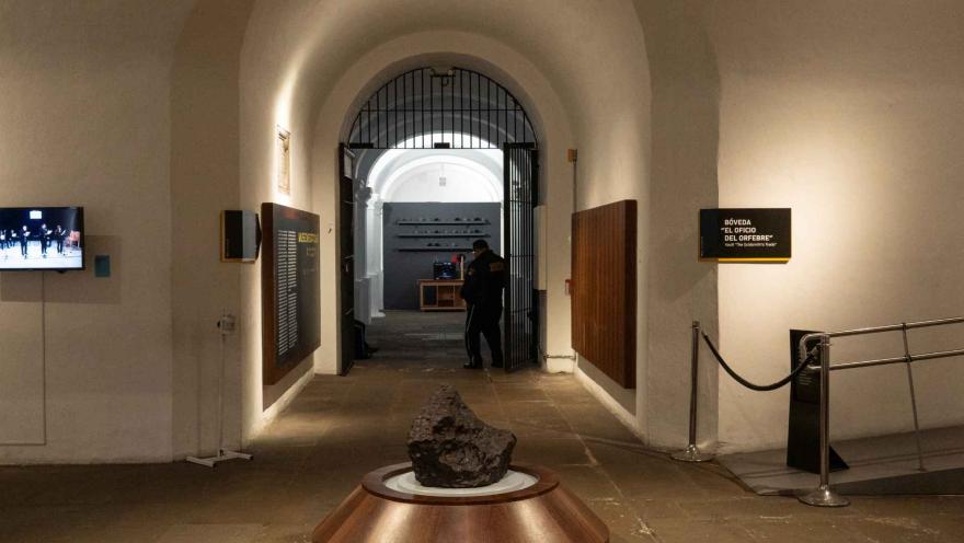  Museo Nacional de Colombia al interior intersección que conduce a un salón ovalado en la que hay una piedra en el centro, un hueco en el techo que hace de ventana cerrada con reja de hierro. Al fondo se ve a un guarda de seguridad.