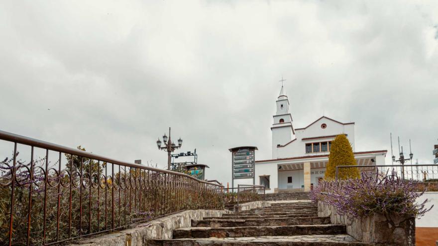  Sendero Cerro Monserrate en el camino de piedra con cerca de hierro llegando a la iglesia bajo un cielo gris.