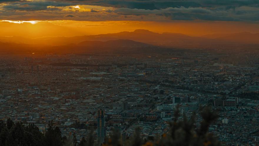 Cerros Orientales con vista de la ciudad en atardecer con cielo naranja y azul, nubes y al fondo la cadena montañosa del occidente.
