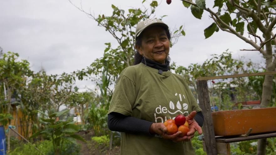  Mujer campesina sonríe y muestra productos cosechados.