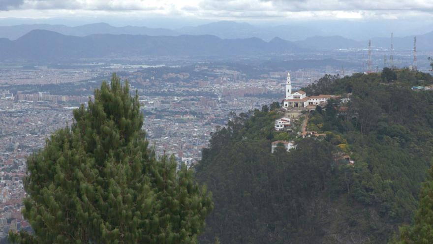  La ciudad de Bogotá desde el cerro de Guadalupe, se ve la iglesia de Monserrate en el cerro de al lado rodeados por grande árboles.
