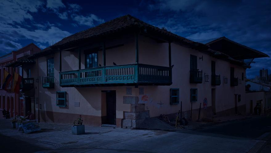 Casa esquinera colonial fachada rosa con balcones verdes, dos palomes sobre el principal y un tono azul como de anochecer. 