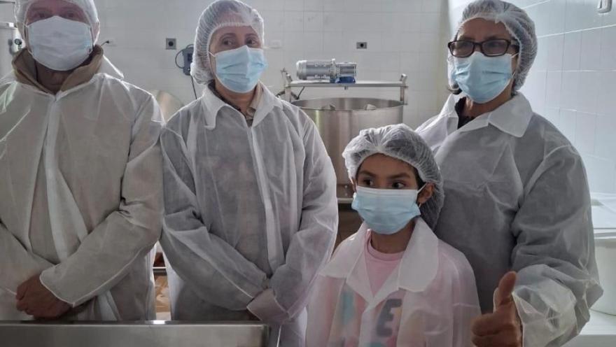 un hombre, dos mujeres y un niño con cofias y tapabocas en una cocina industrial.