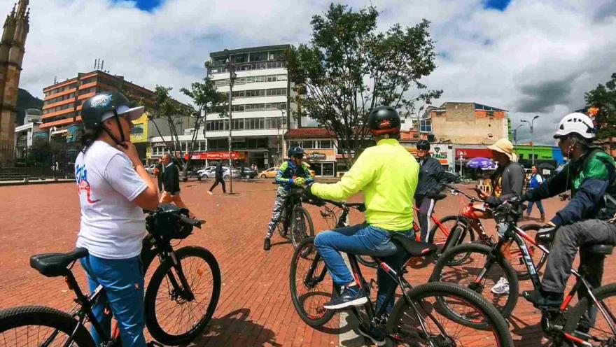 Grupo de ciclistas en la plazoleta de Lourdes, encima de sus bicicletas escucha a un guía.