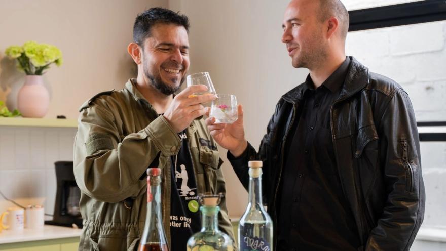 Dos hombres en un salón beben y comparten amenamente delante de tres botellas de trago.