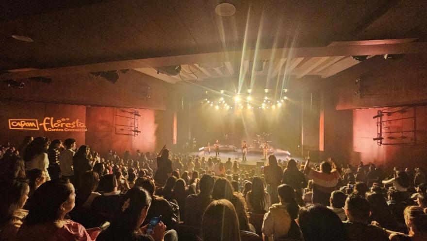 Teatro Cafam interior escenario lleno, semi oscuro con luces reflectivas y un grupo musical en el escenario.  