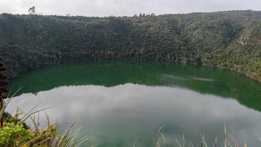 Laguna de Guatavita circular con agua verde y rodeada por frondosa vegetación.