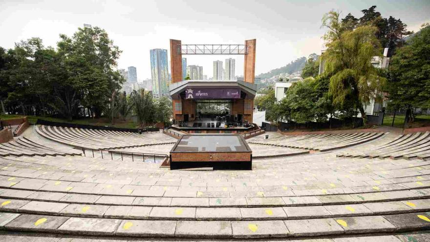 Teatro al aire libre en ladrillo, de día, se ven escalinatas hacia la tarima, que está cubierta por un techo, dos columnas en ladrillo y un aviso gigante donde se lee "Idartes". 