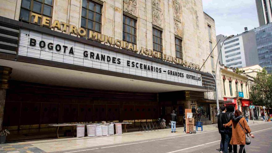 Fachada del teatro Jorge Eliecer Gaitán de día, su puerta y paredes en art decó; el aviso con el nombre en letras en mayúscula y doradas; y el aviso que anuncia las obras en fondo blanco y con letras mayúsculas en color negro. Algunas personas caminan al frente.