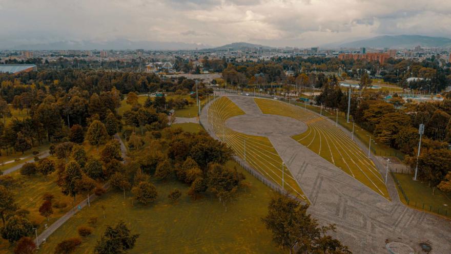 Parque Simón Bolívar plano general desde arriba en dron, se ve la plazoleta de eventos rodeada de árboles frondosos y al fondo edificios de la ciudad y unas cuantas montañas.