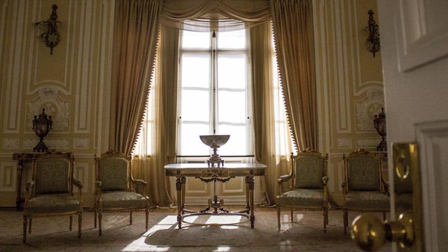 Salón pintado de amarillo con estilo clásico en el que sobresalen 4 sillas y una mesa con un jarrón. Al fondo hay un gran ventanal desde donde ingresa luz natural. 