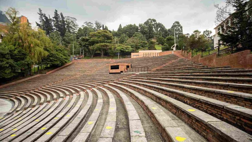 Galería o tribuna en ladrillo en óvalos, rodeada por árboles frondosos.
