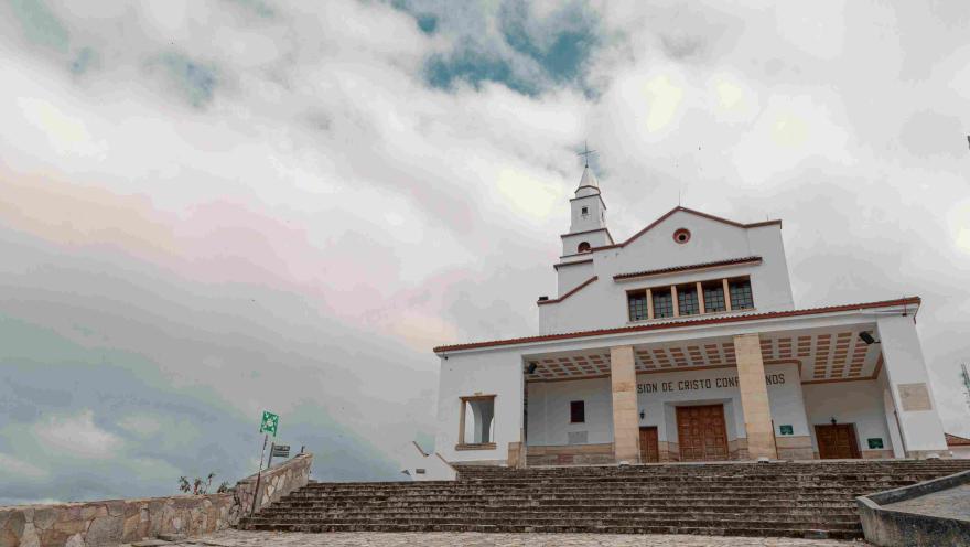 Fachada blanca de la iglesia de Monserrate vista de frente, puertas cerradas y el cielo blanco.