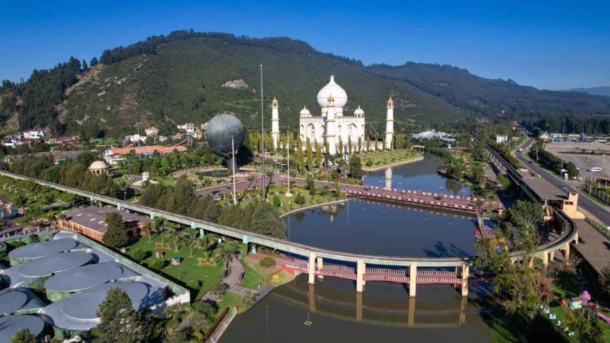 Escultura la Mano de Dios y el monumento del Taj Mahal en el parque, rodeados por lagos y montañas.