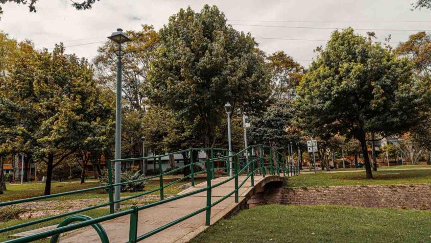 Brick bridge over a water pipe. It is surrounded by metal fences. There are leafy trees around it.