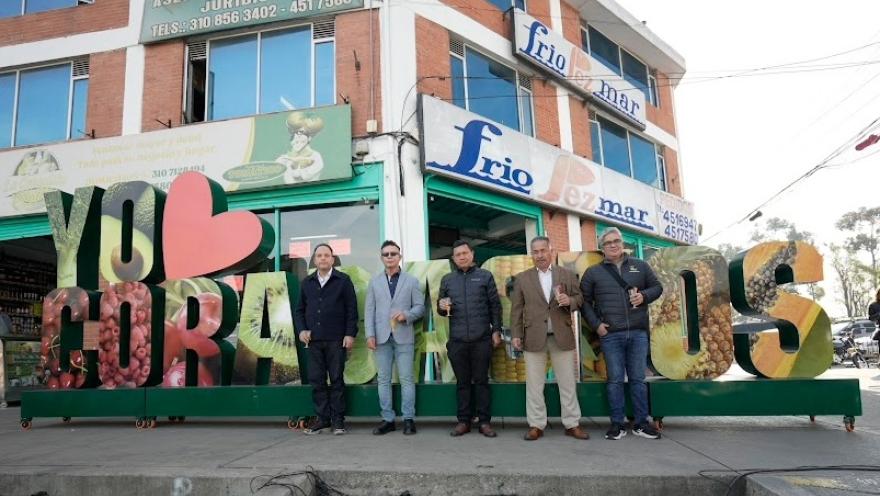 Grupo de hombres adultos parados al frente de un aviso gigante que dice "Yo amo Corabastos". Todos están con una copa en la mano.
