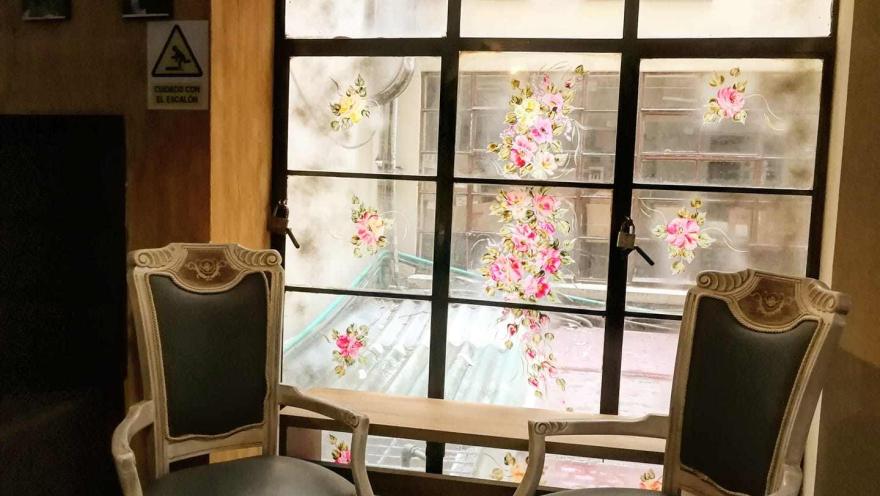 An indoor living room with two antique chairs in good condition and a large window at the back featuring colorful rose designs.