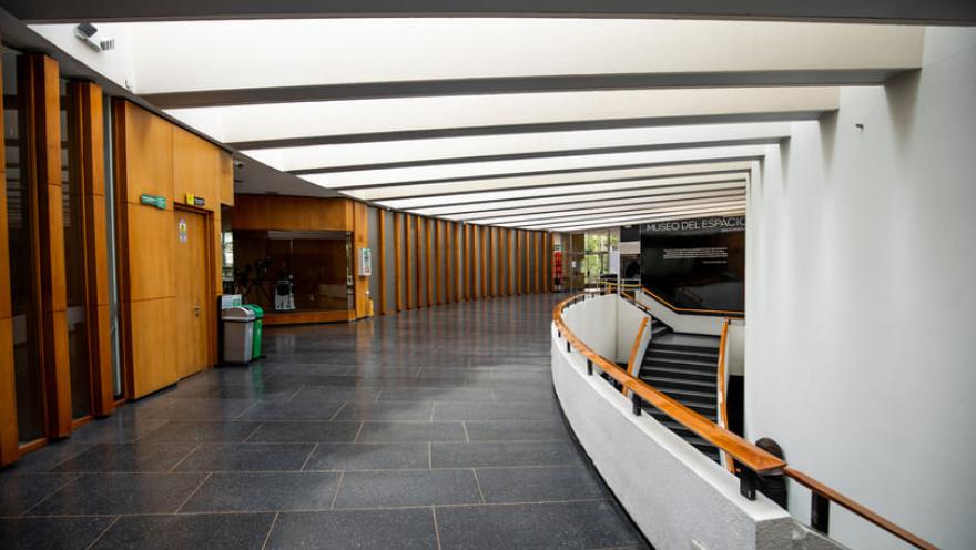  Interior con un salón que parece de biblioteca en el que sobresale un pasillo con paredes en madera, pisos en baldosa negra y paredes blancas. Se ve a la derecha una escalera que conduce a un piso bajo.