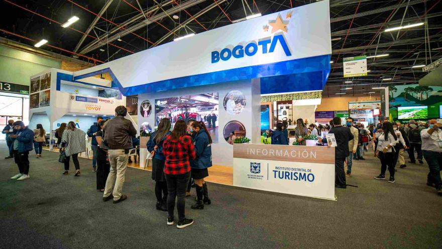 Salón de eventos con un gran stand en el que se lee "Bogotá, Instituto Distrital de Turismo". Hay personas alrededor.