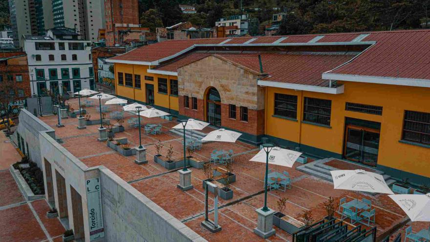 Plaza de Mercado La Concordia vista desde arriba, con varias mesas con parasoles. Al fondo se observan árboles y edificios.