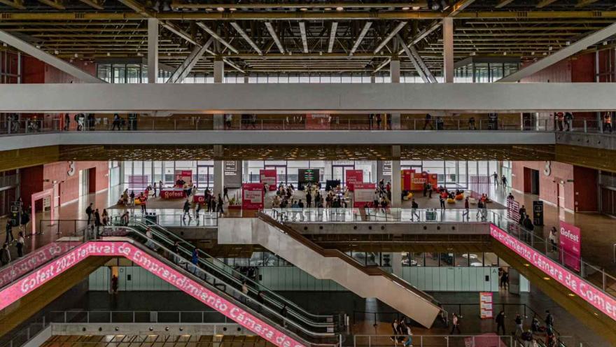 Vista de salón interior con tres pisos y varias escaleras de acceso. Hay una pantalla en led en una de las escaleras donde se lee en letras blancas "Cámara de Comercio de Bogotá"