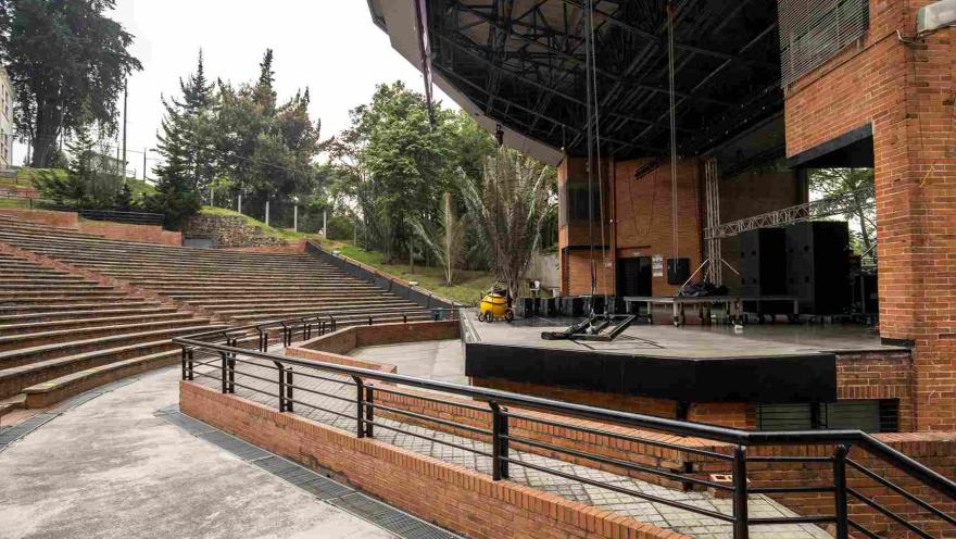 Primer plano de tarima con escenario en el que hay algunos bafles de sonido. Al rededor hay árboles.