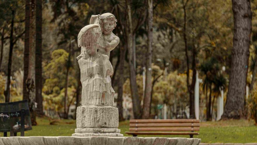 Estructura en piedra tallada rota de un ángel o querubín blanco y que hace parte de una fuente de agua. Al fondo se observan árboles frondosos.