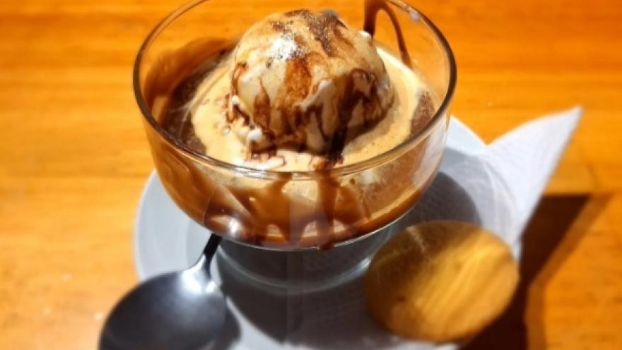 Una copa de helado con café, una galleta dorada y una cucharita, sobre un plato redondo.