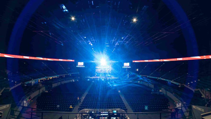 Escenario interno en el que se ven tribunas desocupadas y un haz de luz brillante azul que viene desde la tarima.