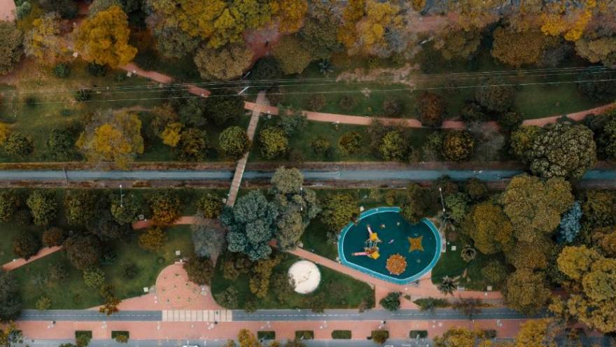 Park seen from above with a long water pipe in the center and a children's playground surrounded by leafy trees.