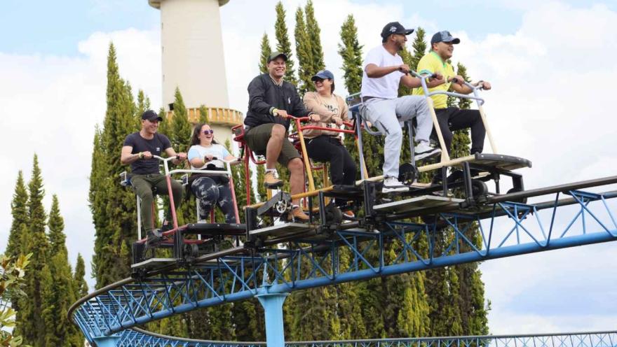 Personas jóvenes ríen montadas en una montaña rusa que conducen pedaleando.