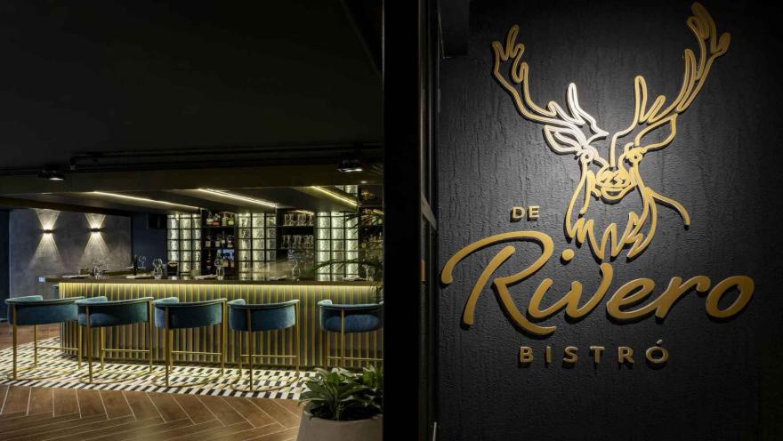 La antesala del sabor. El logo del bistró te guía hacia la elegante barra interior y sillas azules.