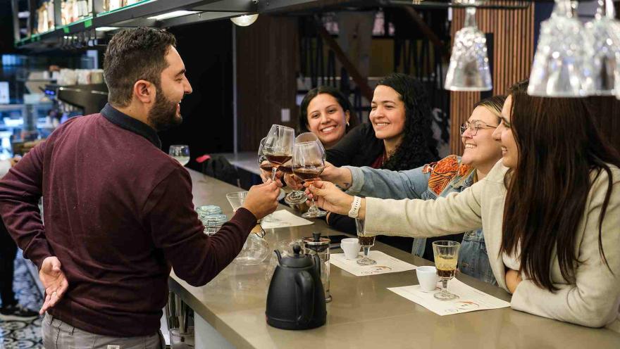 Un grupo de amigos sonrientes brinda con copas de vino o café en una barra de Caffa.