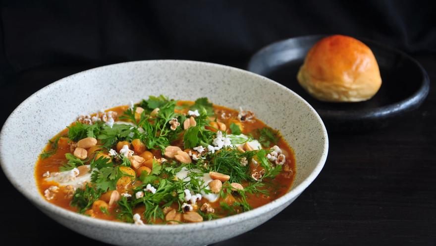 Un tazón de sopa o estofado con garbanzos, cilantro, eneldo y palomitas de maíz, servido con un pan.