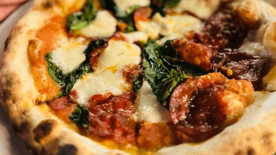 Un primer plano de una pizza artesanal recién horneada con queso derretido, pepperoni y espinacas.