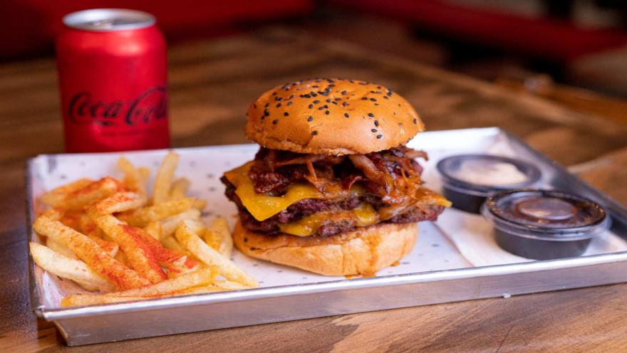 Una jugosa hamburguesa doble con queso y cebolla caramelizada, acompañada de papas fritas y una Coca-Cola.