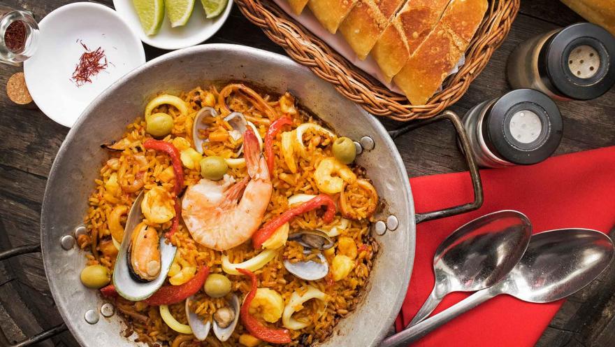 Una vibrante paella de mariscos con arroz, mejillones, calamares y gambas, servida con pan y lima.