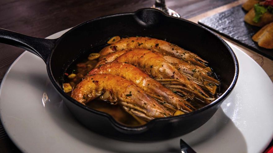 Gambas al ajillo burbujeantes en una sartén de hierro fundido, con un aroma irresistible y listas para disfrutar.