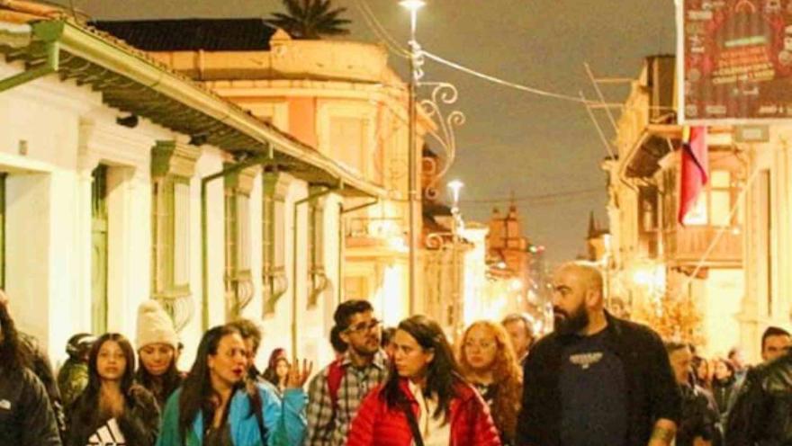 Grupo de personas hombres y mujeres jóvenes camina de noche por entre las calles de La Candelaria. 