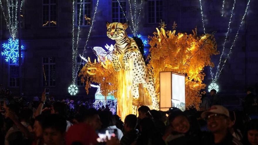 Centenares de personas de noche alrededor de un alumbrado navideño en forma de gran felino.