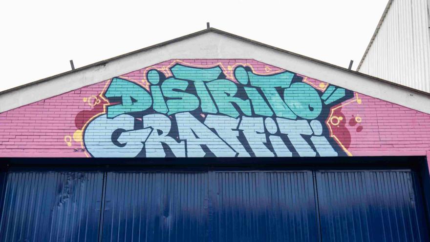 Pared de ladrillo de color rosa encima de una puerta metálica, pintada en color azul con la frase: "Distrito Graffiti".