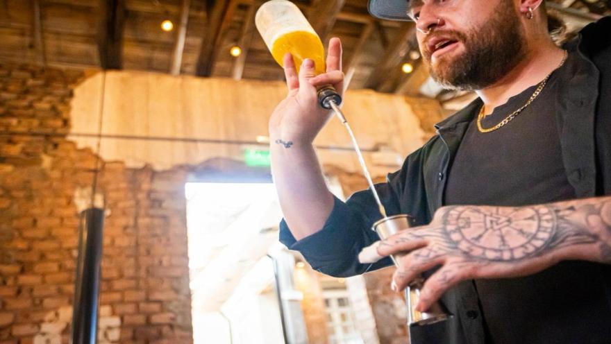Hombre joven que parece un barman haciendo una pirueta con una botella y una copa.