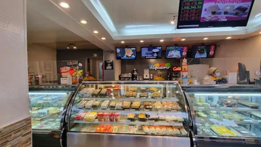 Interior de local comercial donde hay varias vitrinas con jugos y postres. Se observan 5 pantallas de televisión reproduciendo información comercial.
