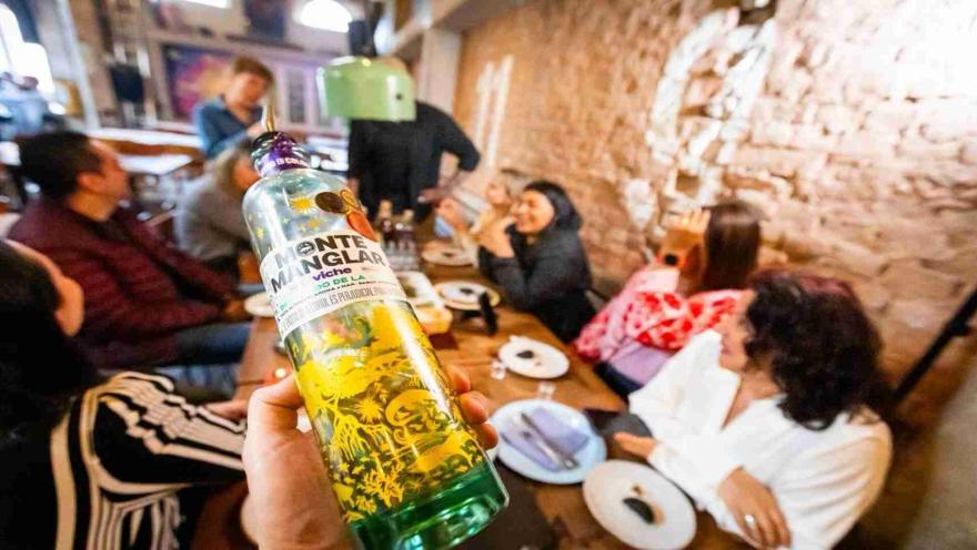 Priemr plano de una botella de licor y de fondo unas personas sonriendo.