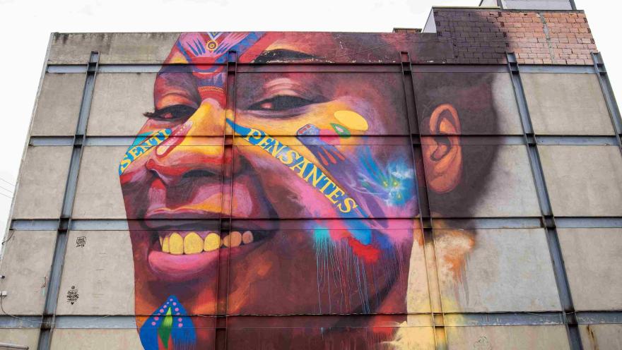  Pared de ladrillo de color blanco con el rostro sonriente de una mujer joven afro. En el rostro hay dos palabras: "Senti y Pensantes".